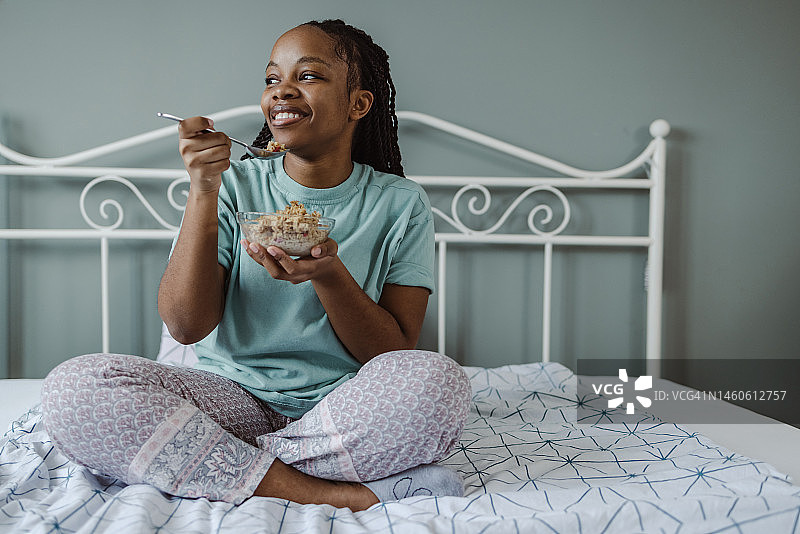 快乐的非裔美国妇女在卧室吃麦片图片素材