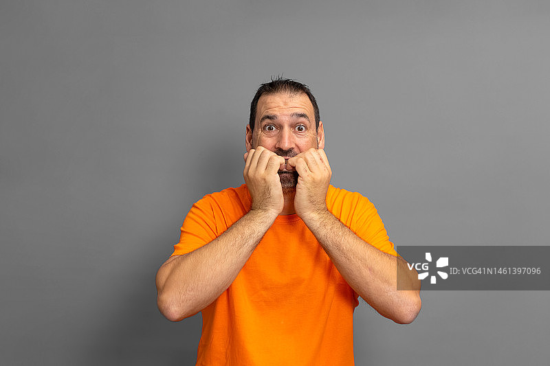 一个穿着橙色t恤，留着胡子的拉丁裔男人在咬指甲图片素材