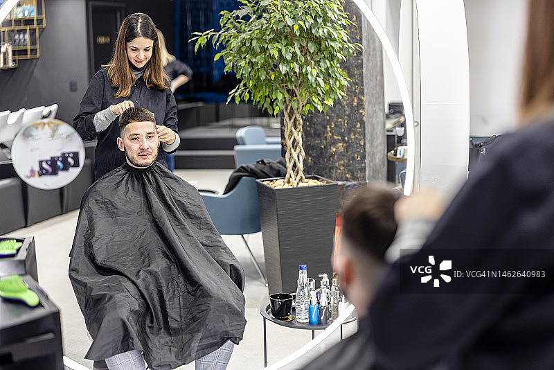 一个年轻人坐在理发店里理发。图片素材