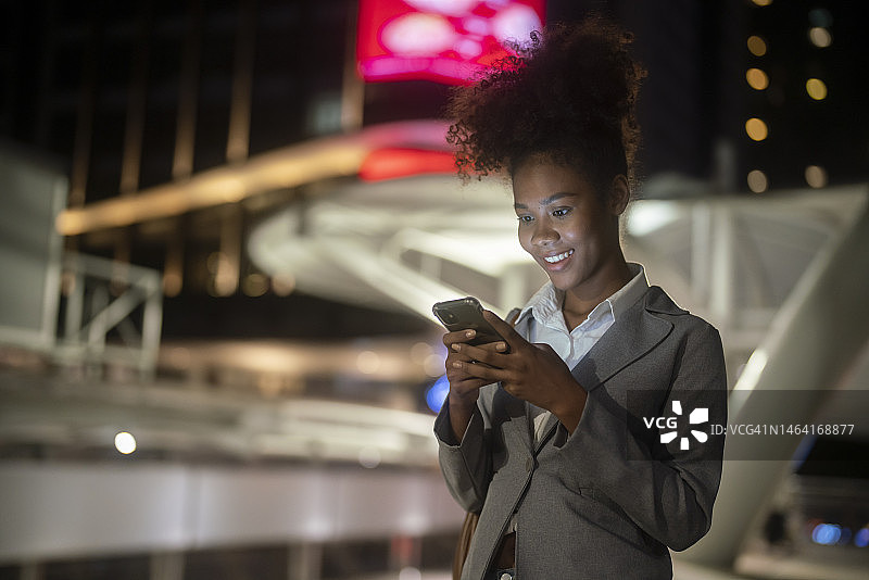 一名年轻女子在霓虹灯闪烁的夜晚街道上用智能手机漫步图片素材