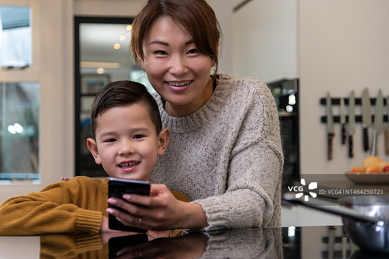 快乐的亚洲母亲和儿子在家里看智能手机图片素材