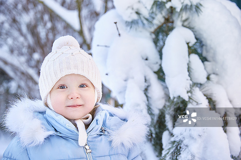 俄罗斯，一个阳光灿烂的日子，穿着蓝色夹克、戴着针织帽的小男孩站在白雪覆盖的森林或公园里图片素材