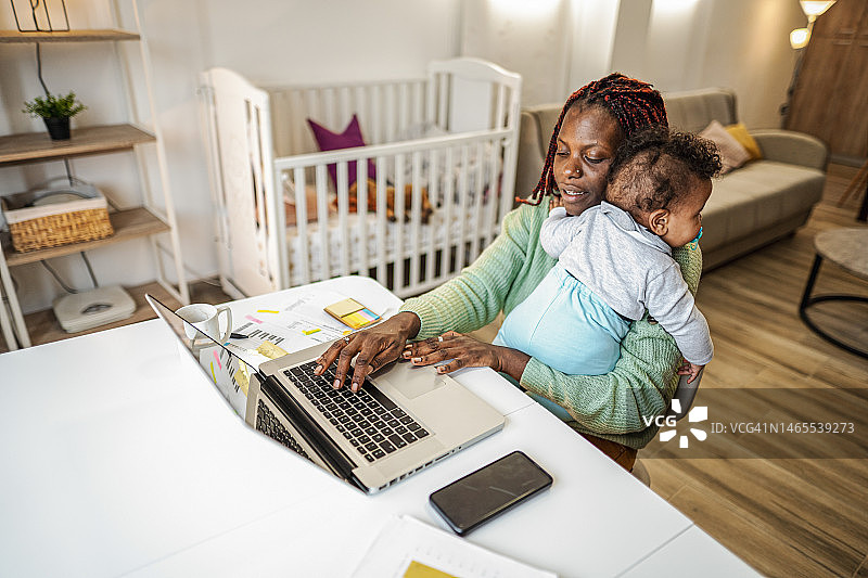 努力工作的黑人母亲一边在家做生意一边照顾她的小婴儿图片素材