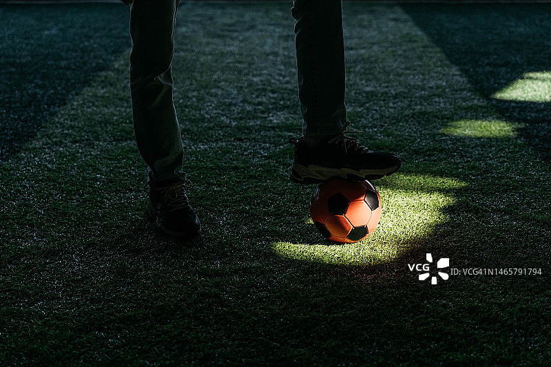 在绿色草坪上的一束光中踢足球。黑暗的背景。图片素材
