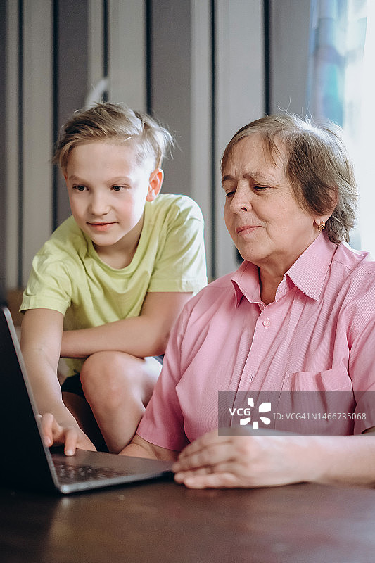 一个10岁的男孩帮助一位老妇人网购。孙子教奶奶如何使用笔记本电脑图片素材