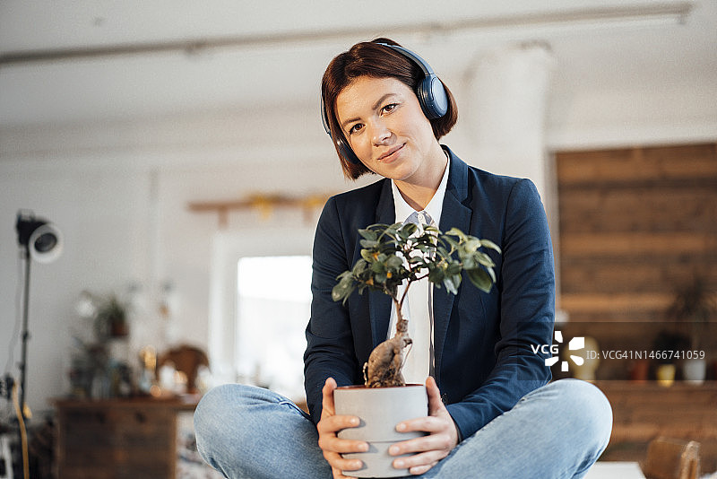 微笑的女商人与盆栽植物听音乐通过耳机在办公室图片素材