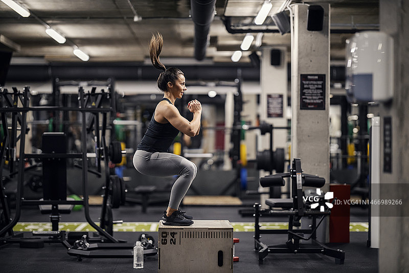 一个强壮的女运动员正在体育馆里做箱子跳跃。图片素材