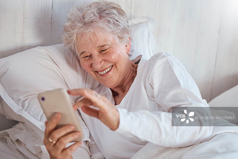 快乐的老妇人，床上或电话上的社交媒体上的表情包，漫画或笑话在互联网上。高级女士，卧室或智能手机技术与笑在社交网络，有趣的视频或电子邮件上的网页，应用程序或在线图片素材