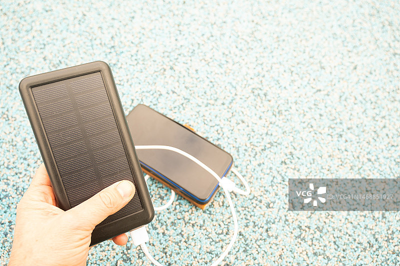 一个人拿着太阳能充电宝，用电缆给手机充电。图片素材