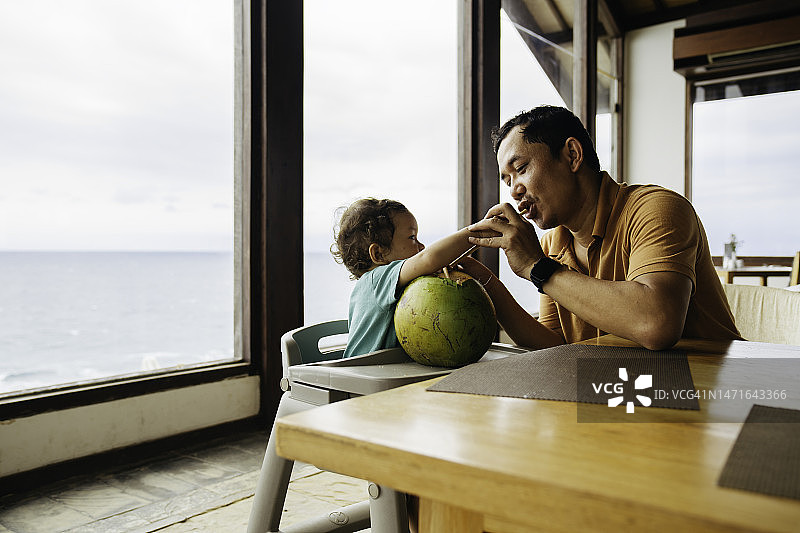 亚洲男人和他的儿子坐在桌子上喝椰子水图片素材