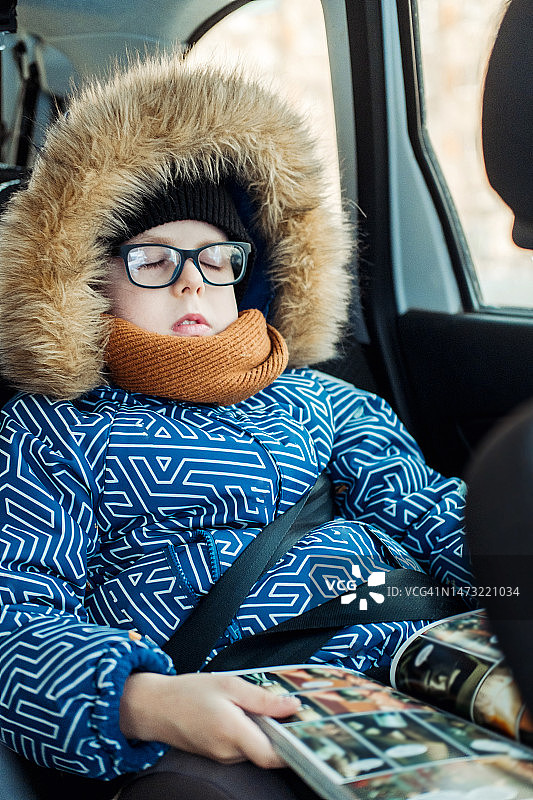 一个8岁的男孩，戴着眼镜，穿着冬季夹克，在车里靠窗看书图片素材