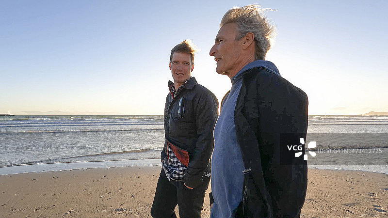 父亲和成年儿子在海滩上散步聊天图片素材