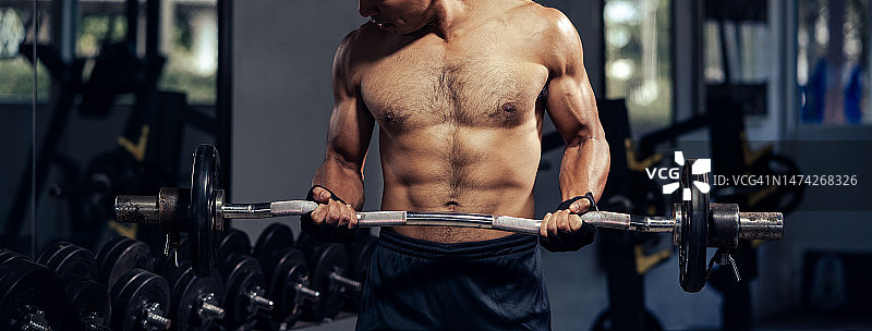 强壮的健美运动员在健身房用杠铃锻炼二头肌。图片素材