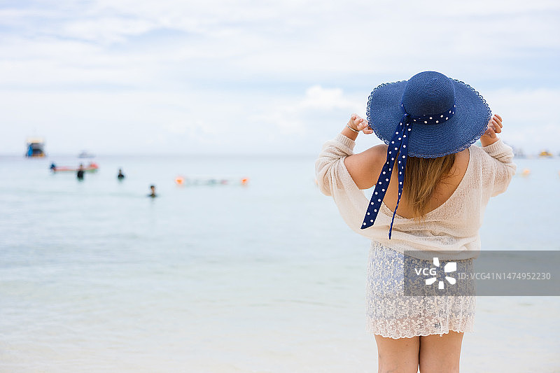 亚洲年轻的超大女人戴着帽子，站在海滩上。图片素材