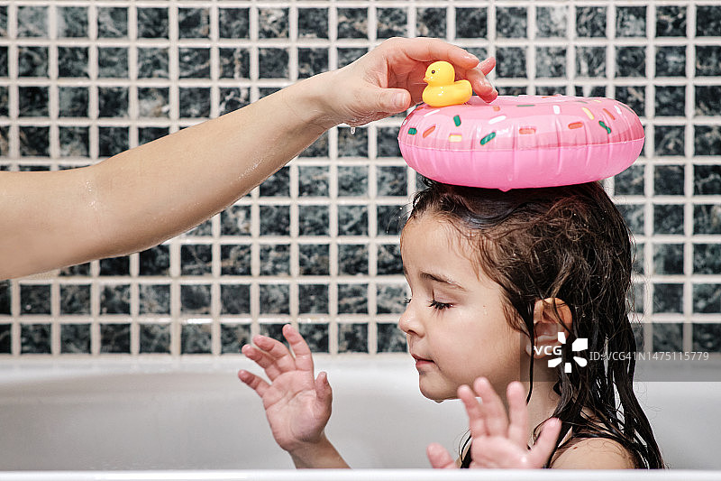 在浴缸里，母亲把洗浴玩具放在女儿的头上图片素材