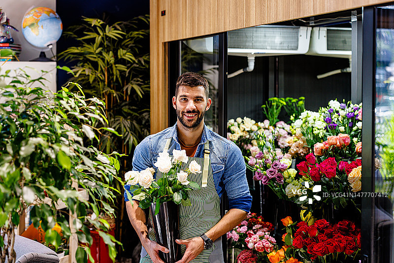 一位在花店工作的成功男性工人正捧着鲜花。图片素材