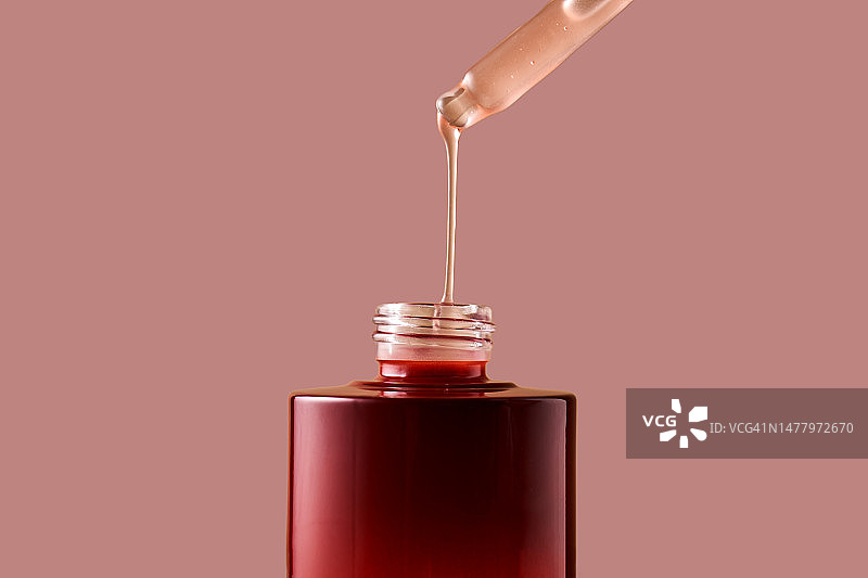 一滴粉红色的化妆品从滴管滴进了一个紫红色的瓶子里。图片素材