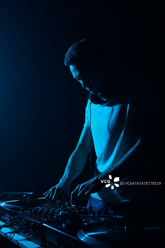 电子音乐DJ在夜总会演奏音乐的剪影。酷酷的年轻白人在舞台上混音图片素材