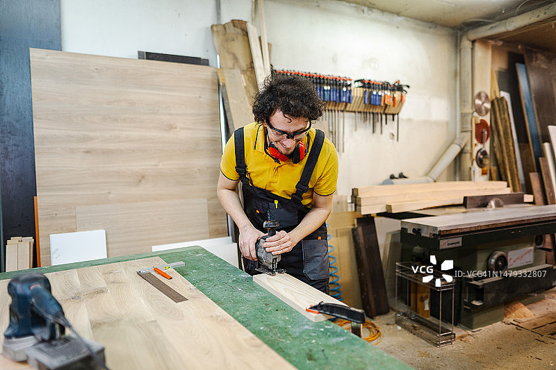 木工在木工车间用电动拼图工具切割胶合板图片素材