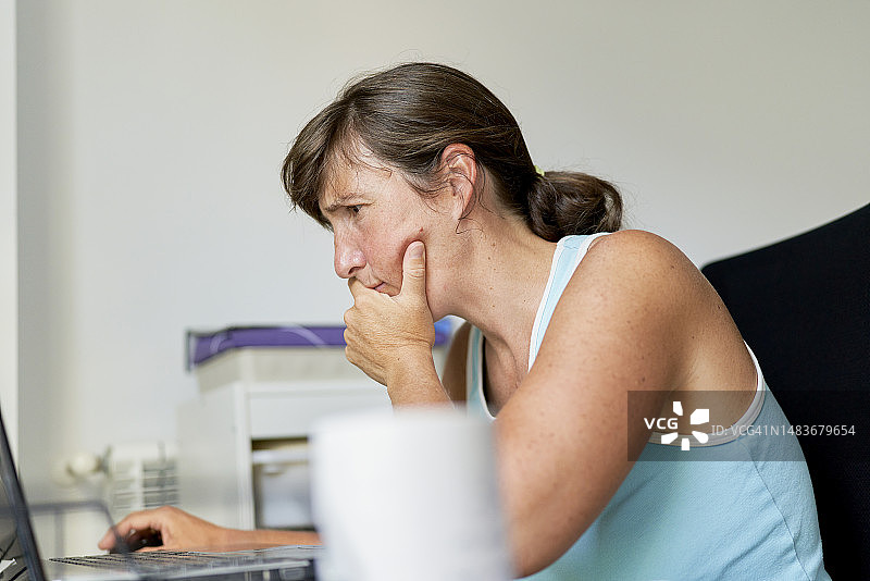 一个穿着便服的女人坐在家里的办公桌前，背对着相机看电脑图片素材