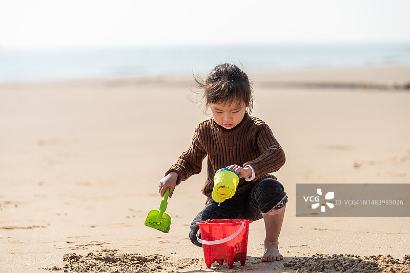 一个女孩在沙滩上玩沙子制作塑料工具图片素材
