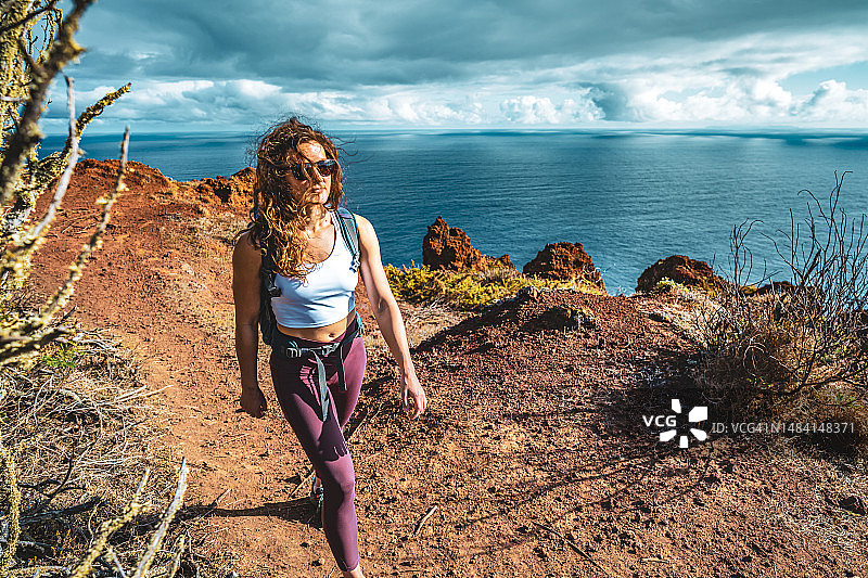 一名背包客女子喜欢在早晨沿着陡峭的悬崖徒步旅行，俯瞰大海和马德拉海岸崎岖的山麓。Ponta do Bode，马德拉岛，葡萄牙，欧洲。图片素材