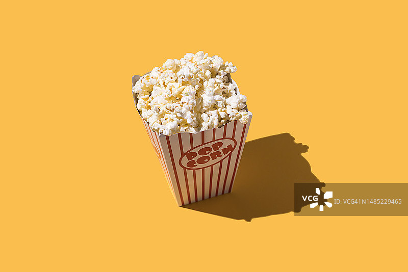 爆米花在纸板桶与白色和红色装饰在黄色背景。电影院，娱乐，电影，演出，肥胖，不健康食品，快餐和肥胖的概念。图片素材