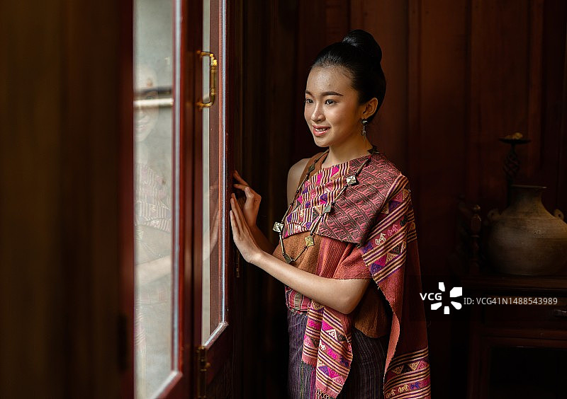 穿着传统老挝服装的美丽亚洲老挝妇女透过窗户向外看图片素材