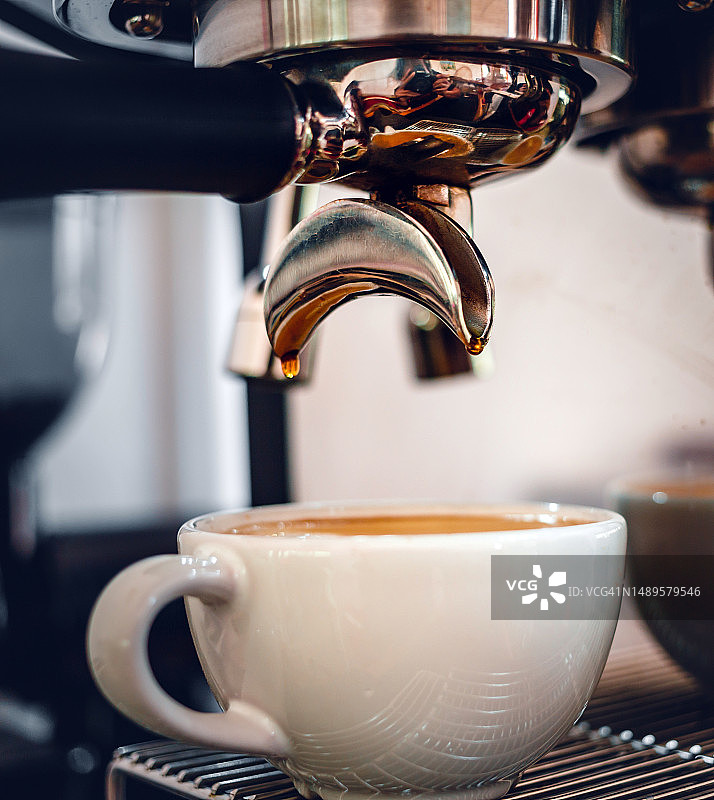 浓缩咖啡从一个专业的咖啡机与无底过滤器提取，特写从咖啡机的咖啡滴图片素材