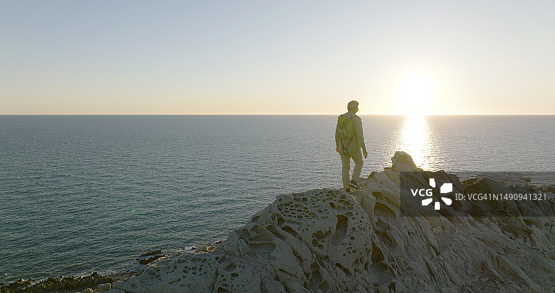 日落时分，一个人在海上的山脊上探险图片素材