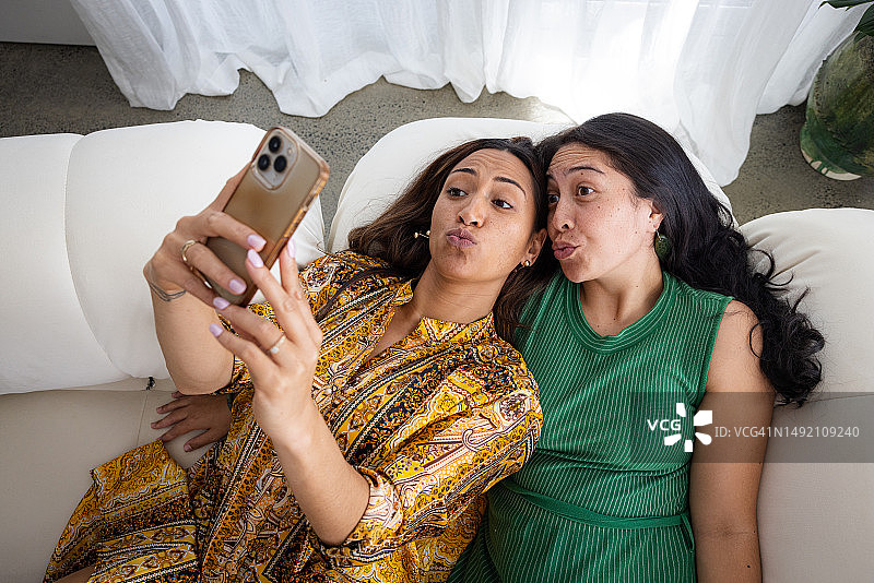 两个长头发的女人躺在一起，嘟着嘴笑着玩手机图片素材