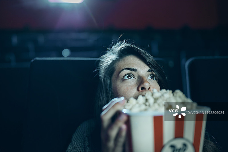 在电影院边看电影边吃爆米花的恐惧女人。图片素材