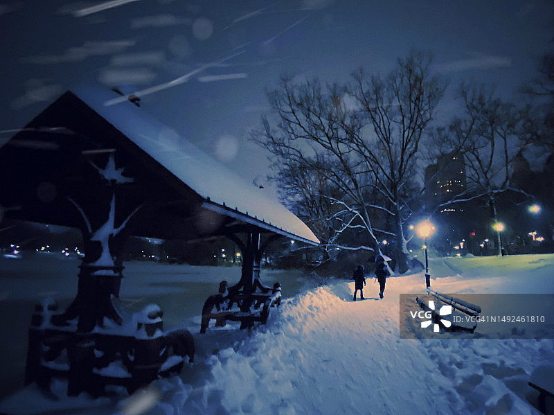一对夫妇在晚上的暴风雪中沿着纽约市中央公园的湖边散步图片素材