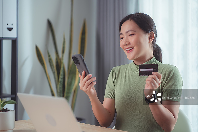 亚洲女性喜欢在家里用信用卡和智能手机进行网上购物。图片素材