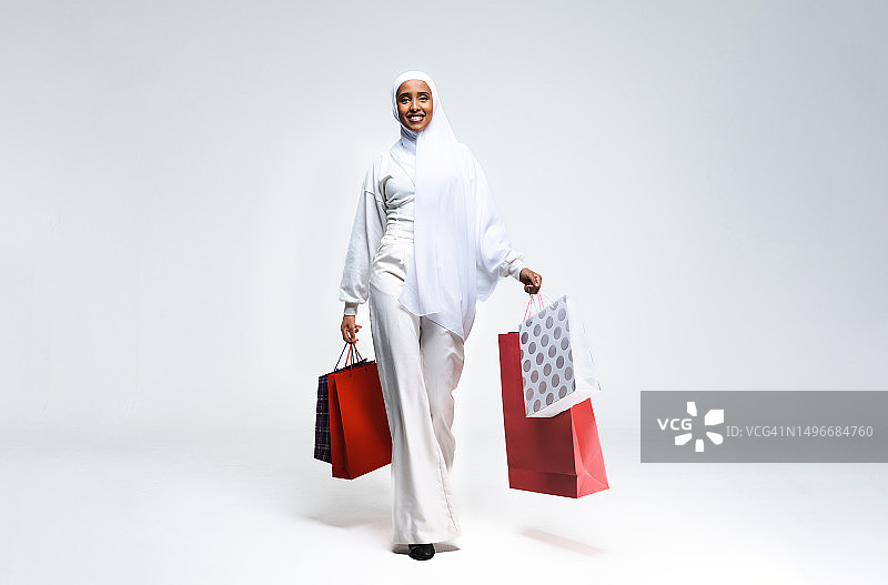 阿拉伯联合酋长国，一个微笑的女人拿着购物袋站在白色背景下图片素材