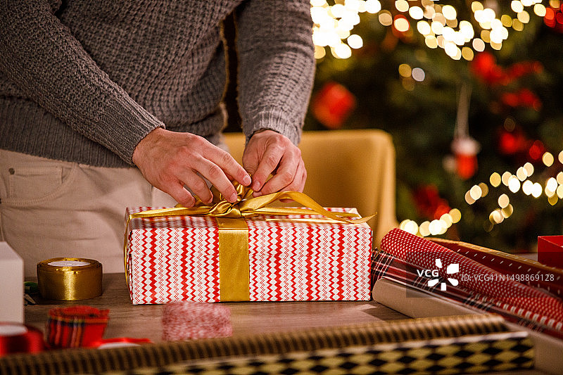 一个年轻人把一个金色的蝴蝶结放在他包好的圣诞礼盒上图片素材
