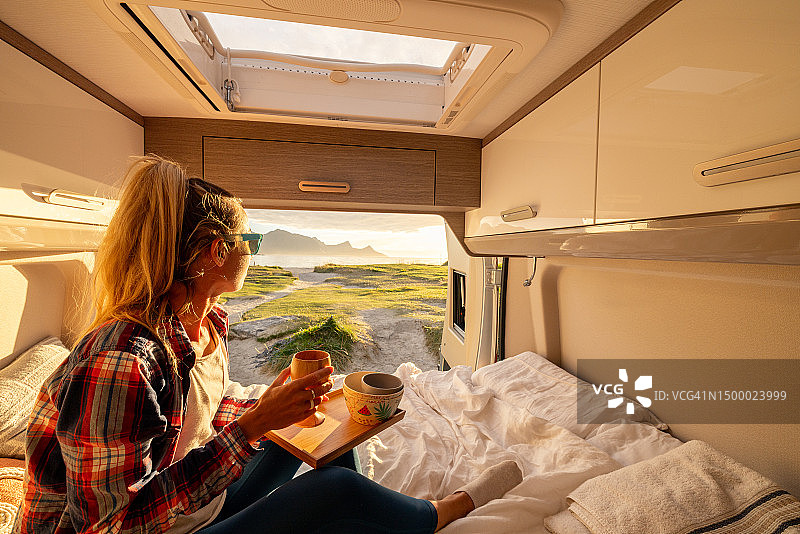 日落时分，女人在她的露营车后面放松，面包车生活概念。图片素材