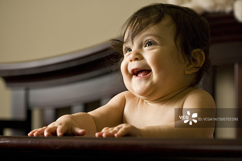 一个大眼睛的婴儿抱着婴儿床的栏杆微笑着图片素材