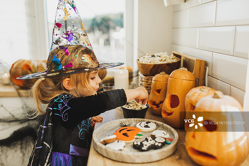 穿着女巫服装的女婴偷吃万圣节桌上的糖果。快乐的童年图片素材