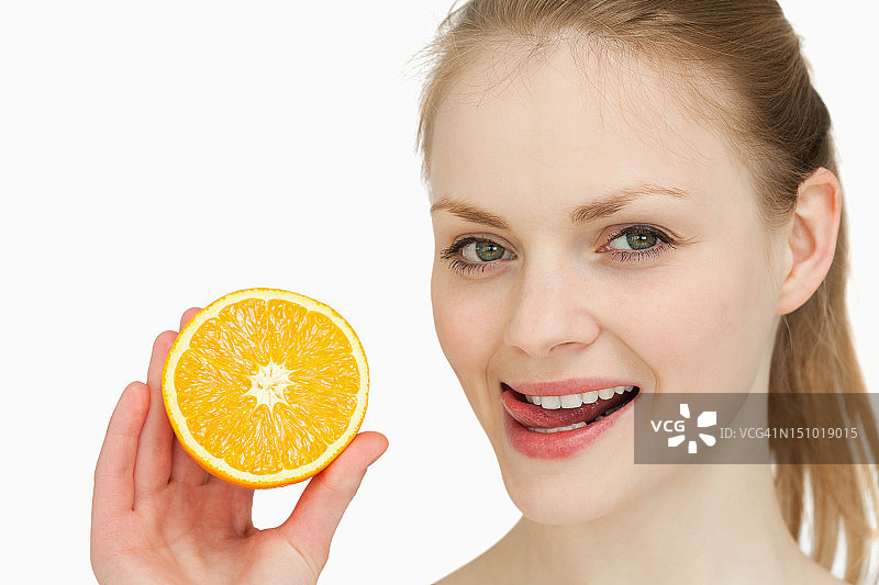 一个女人拿着一个橙子，把舌头放在嘴唇上图片素材