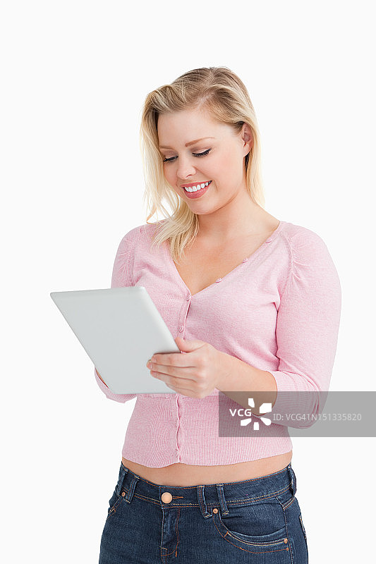 微笑的金发女人站着，触摸着她的平板电脑图片素材