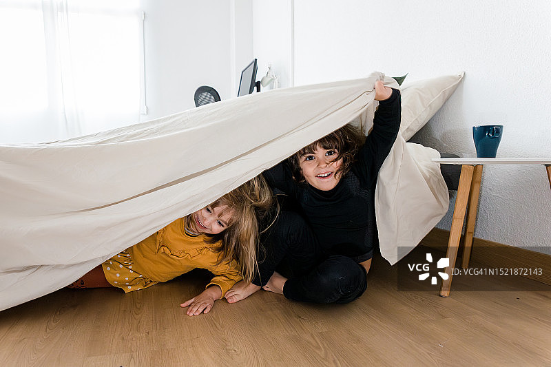 两个孩子躲在家里卧室的床底下玩。图片素材