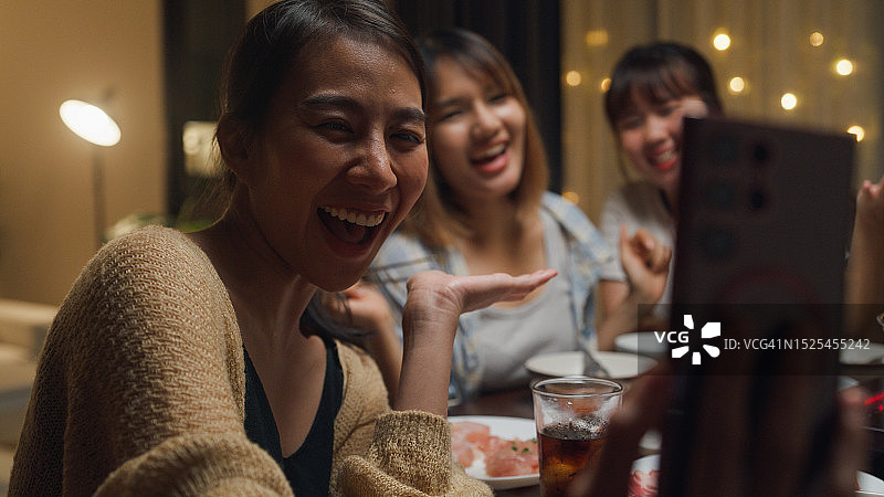 一群快乐的亚洲朋友一边吃火锅一边自拍视频通话，晚上在家里聚在一起吃春节团圆饭。生活方式享受美食。图片素材