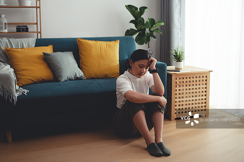 一个亚洲女人坐在家里，抱着膝盖思考着孤独的问题。图片素材