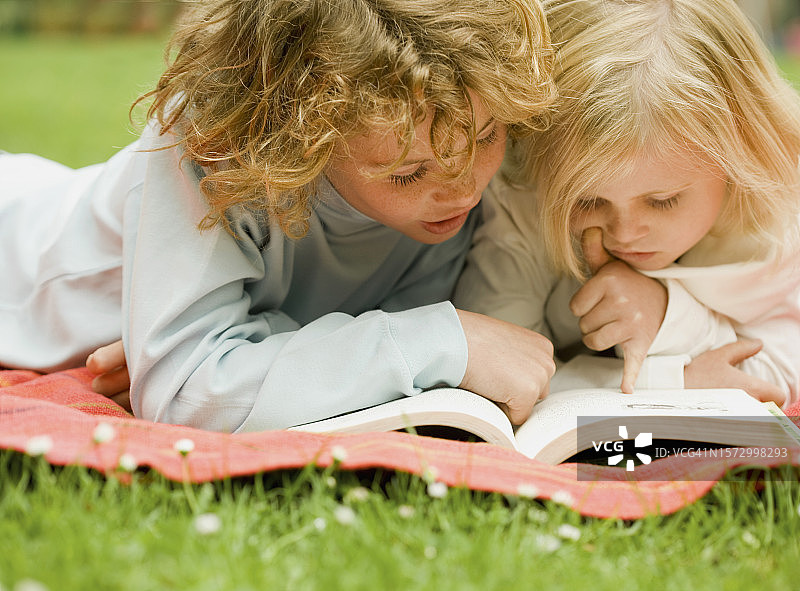 两个孩子躺在花园里看书图片素材