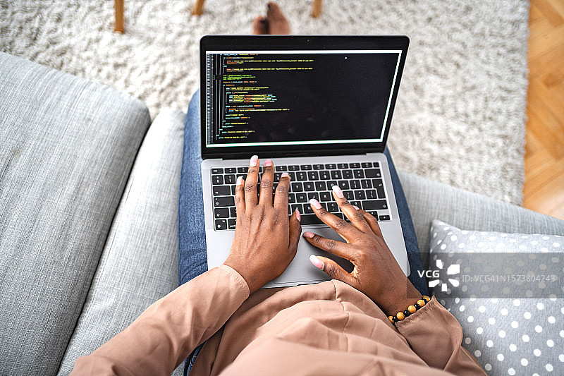 一位黑人女性坐在客厅的沙发上，用笔记本电脑输入密码图片素材