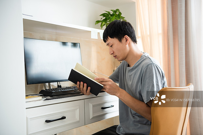 亚洲人在家工作，坐在电脑前看书，享受休息图片素材