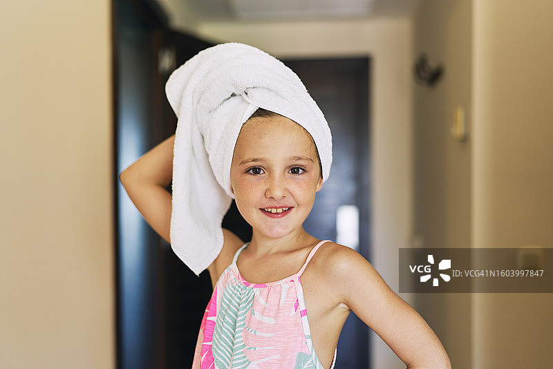 一个美丽的女孩站在酒店房间里，头发上缠着毛巾，微笑地看着镜头，正面视图图片素材
