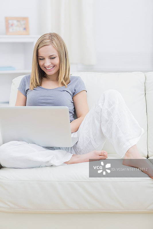 轻松快乐的女人在沙发上使用笔记本电脑图片素材