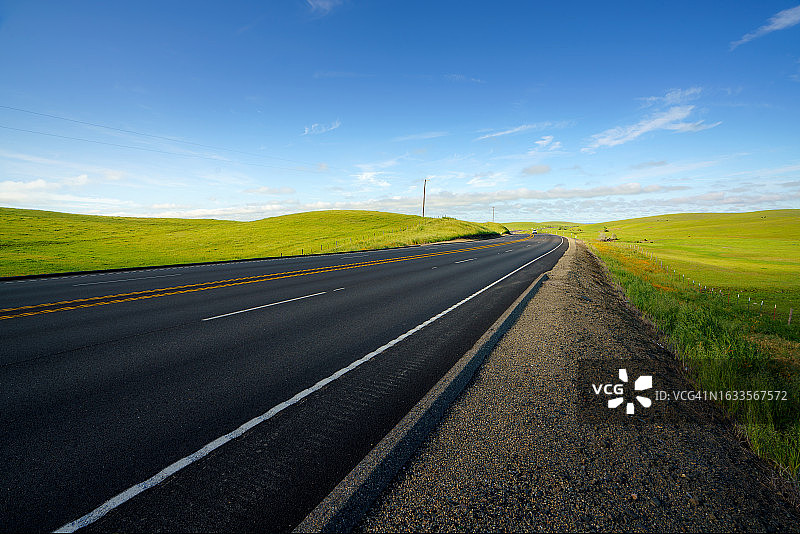 汽车行驶在以牛场、草地、小溪和山脉为背景的美国乡村道路上。图片素材